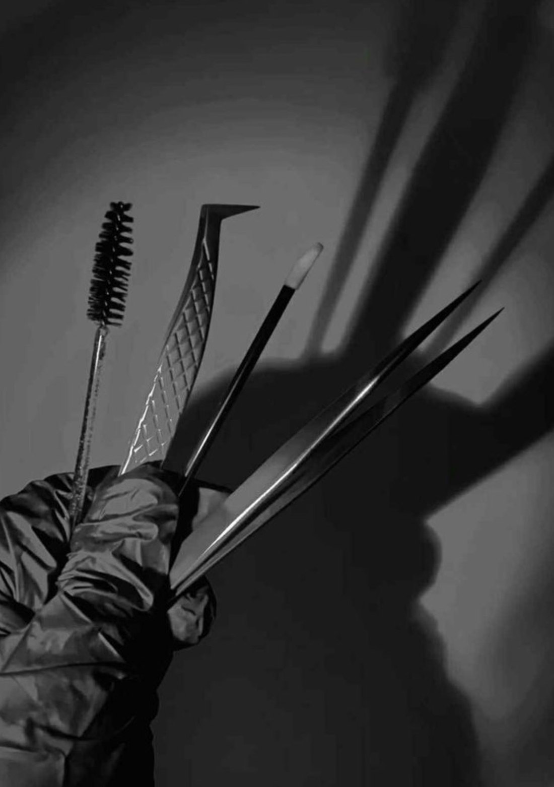 Main gantée tenant les outils de pose d'extensions de cils : goupillon, pinces de précision et applicateur